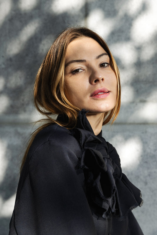 Woman wearing a black outfit with ruffled details against a gray wall.