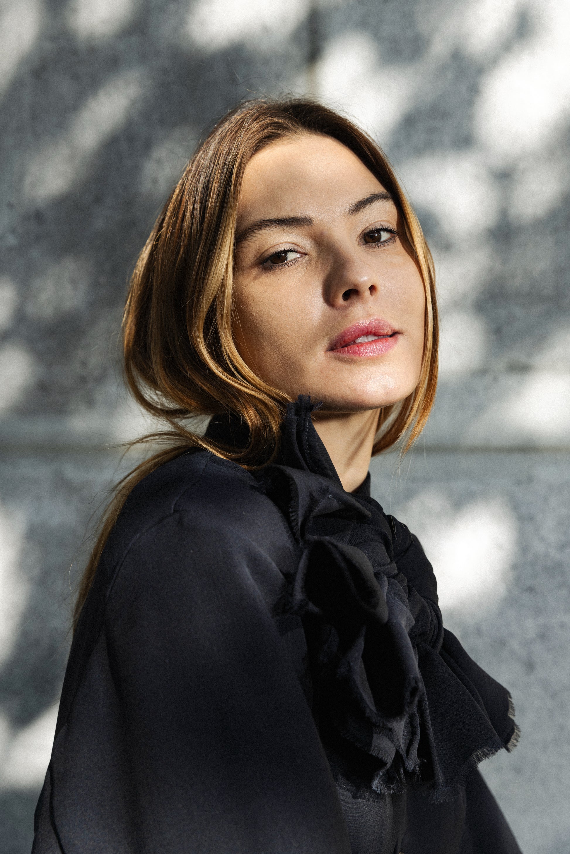 Woman wearing a black outfit with ruffled details against a gray wall.